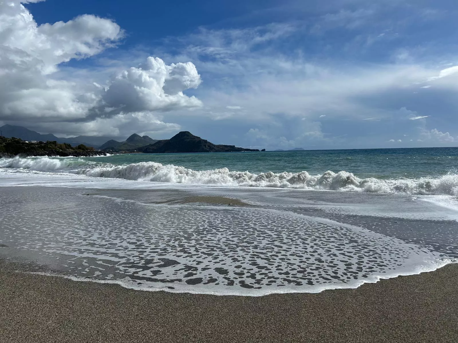 Wellen am Strand mit Blick auf Berge und dramatischem Himmel