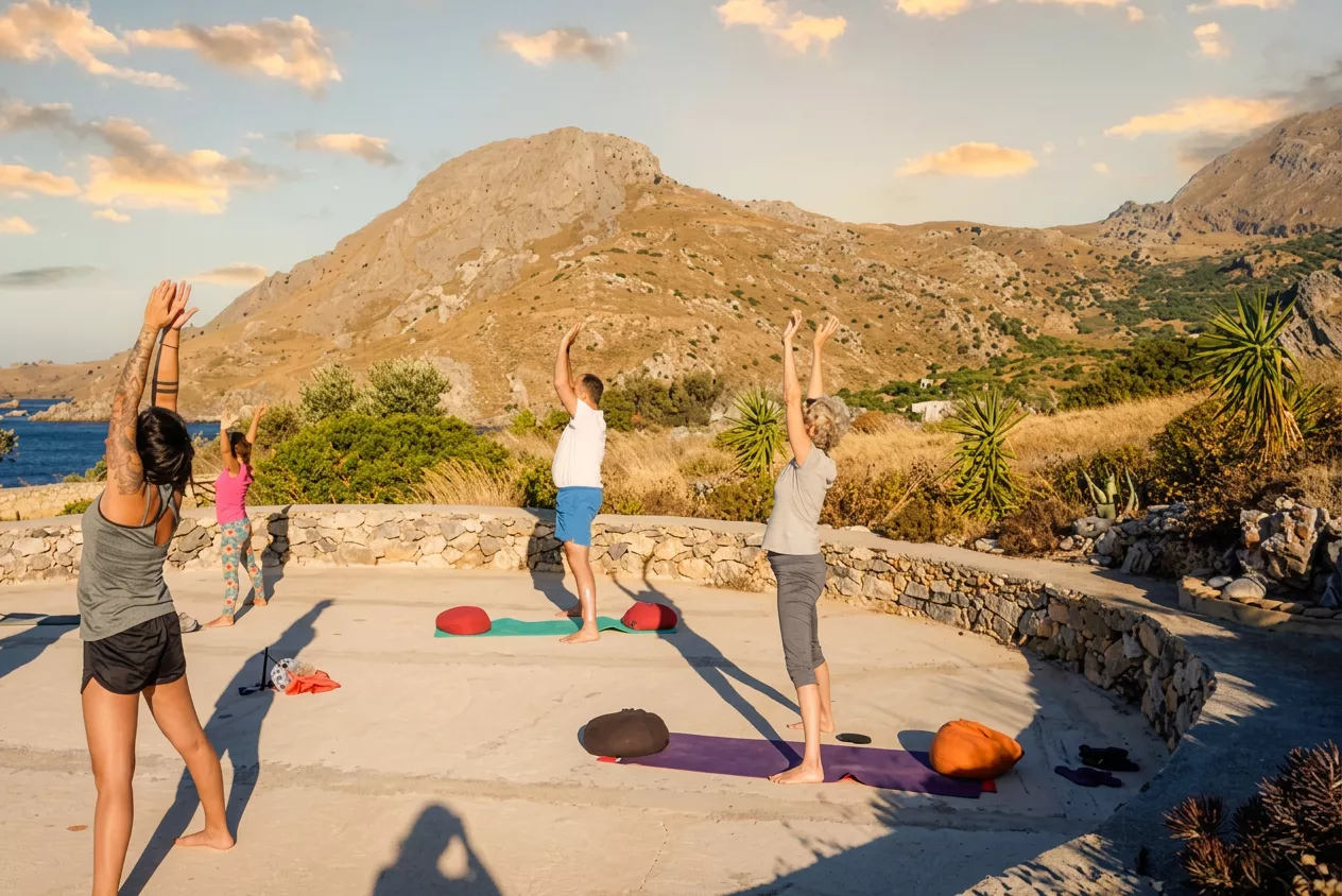 Yoga-Gruppe bei Sonnenuntergang auf einer Terrasse mit Blick auf Berge und Meer